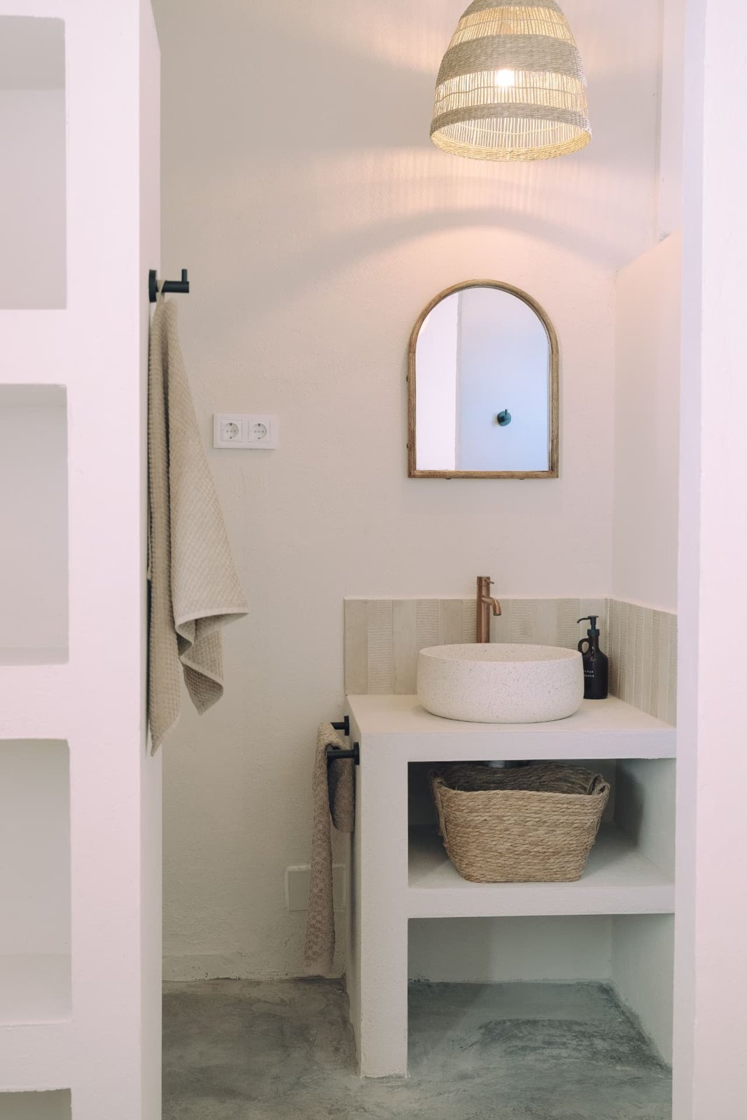 Ensuite bathroom with terrazzo basin, arched mirror and rattan pendant
